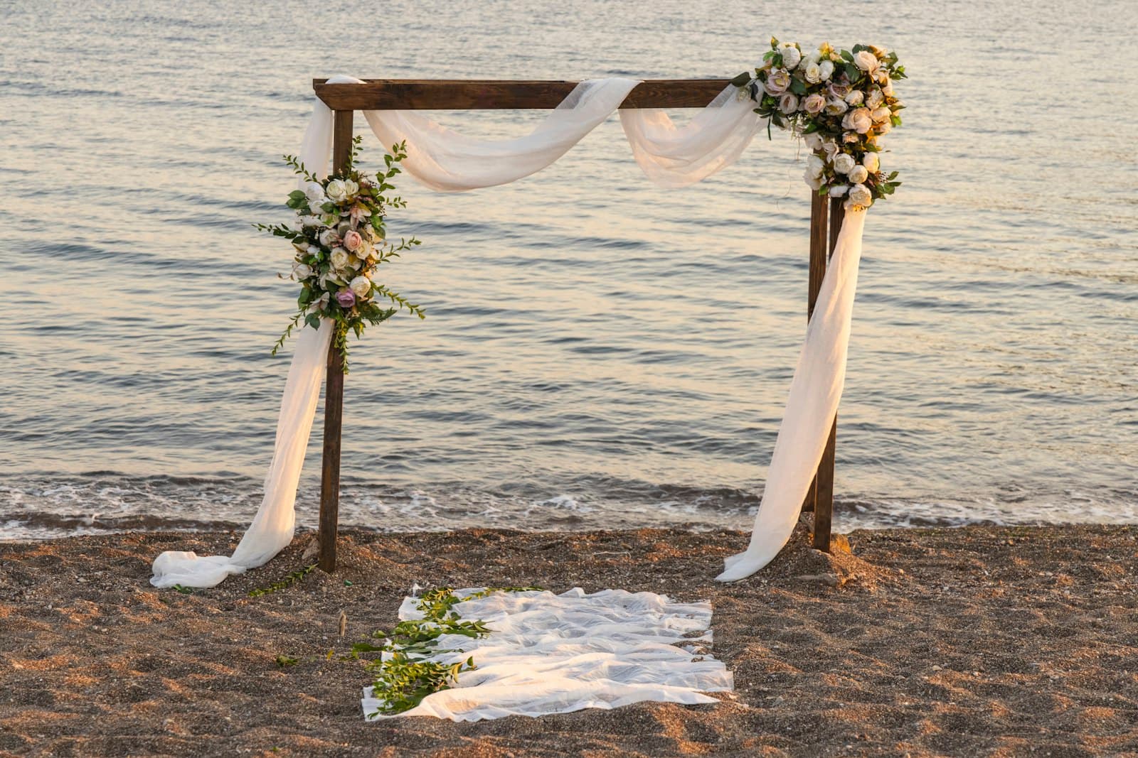 Wooden wedding arch draped in white fabric on a sandy beach