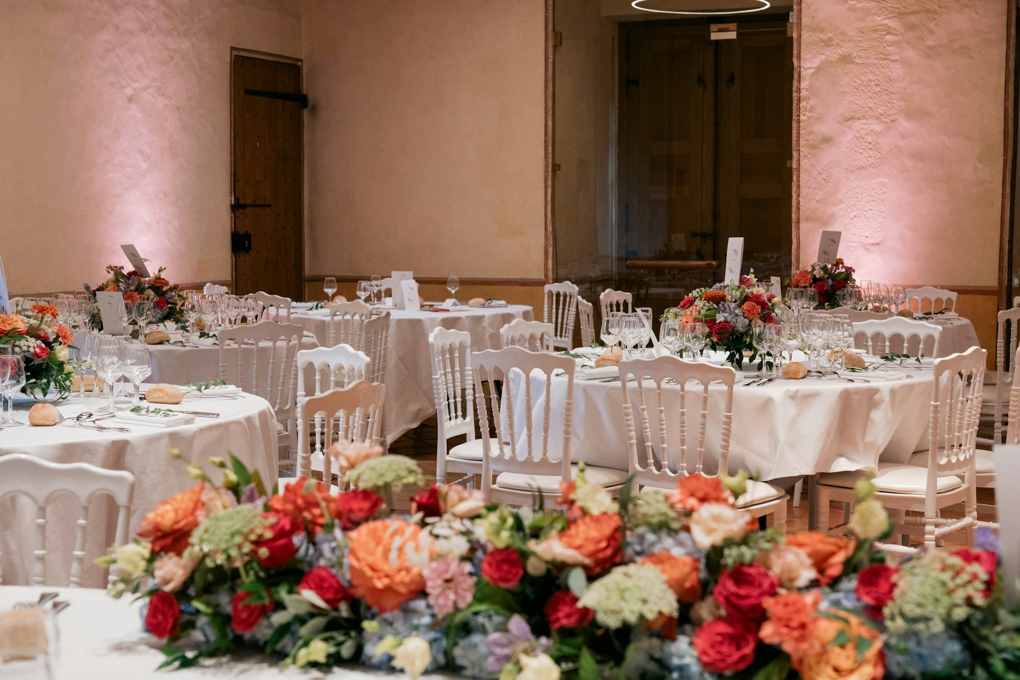 Wedding reception room with round tables, white chairs and colorful floral centerpieces