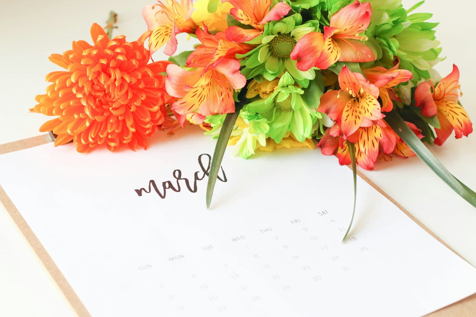 Printed monthly calendar page beside a bunch of orange and green flowers
