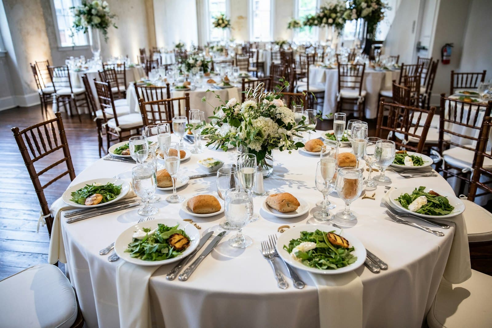 Round reception table set with plated salads in a bright ballroom