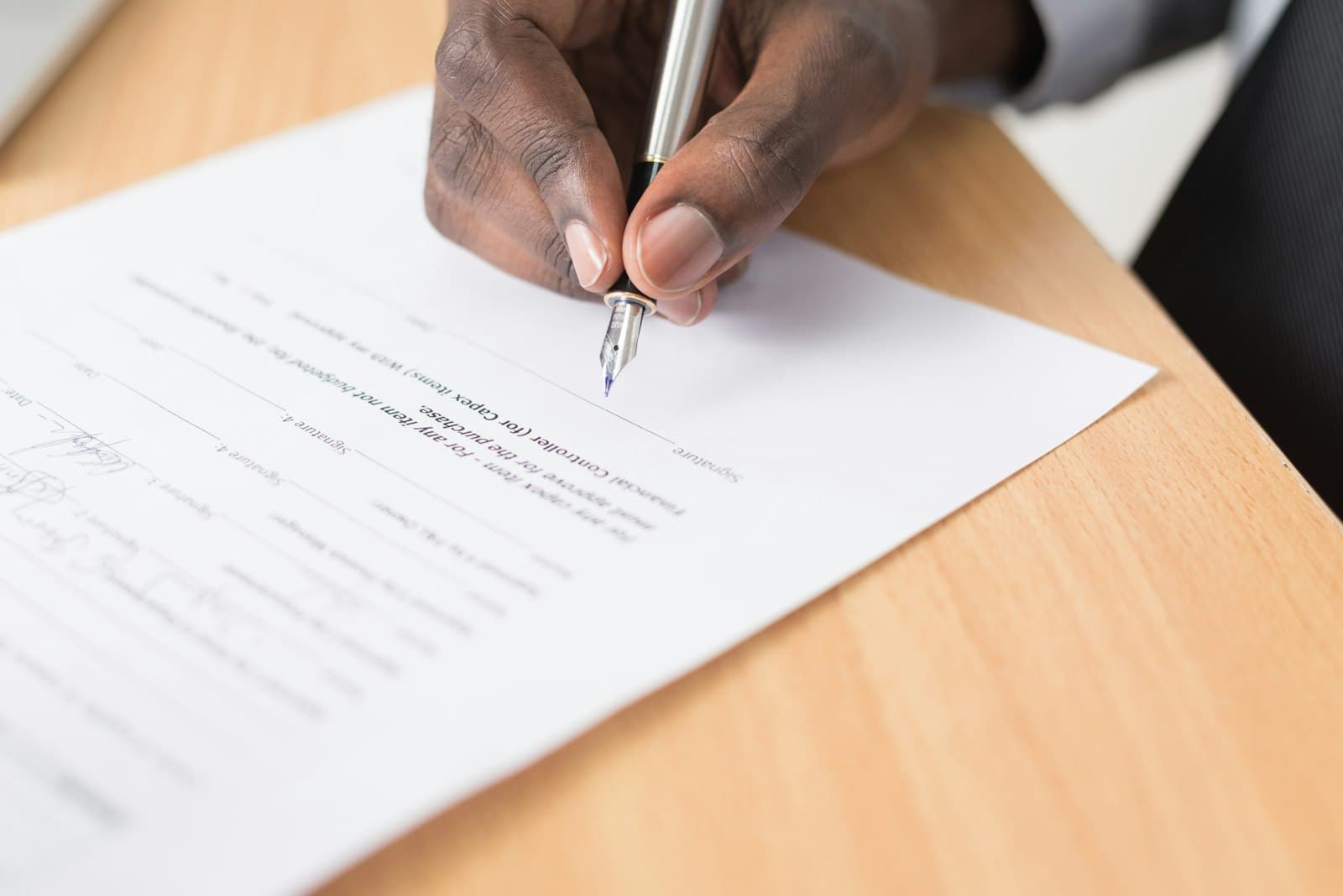 Hand signing a document with a pen on a wooden desk
