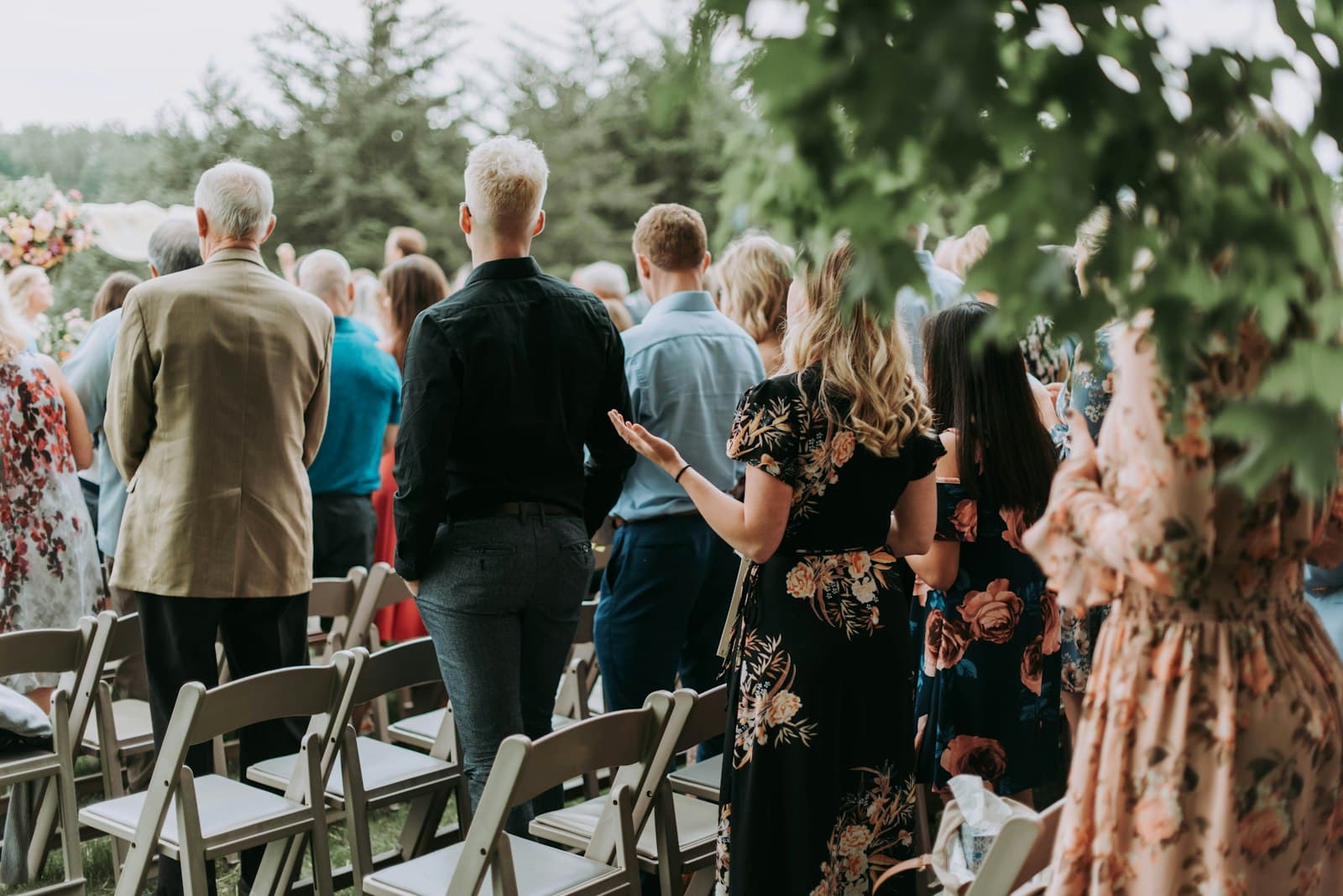 Wedding guests standing at an outdoor ceremony, seen from behind
