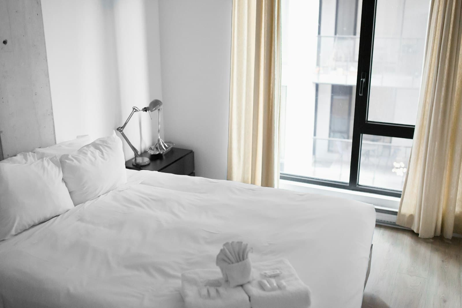 Hotel bed with white linens beside a large window