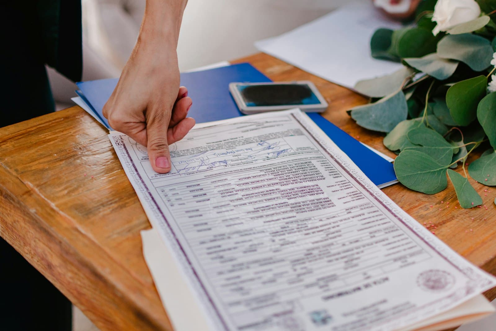Hand pointing at a marriage certificate on a wooden table