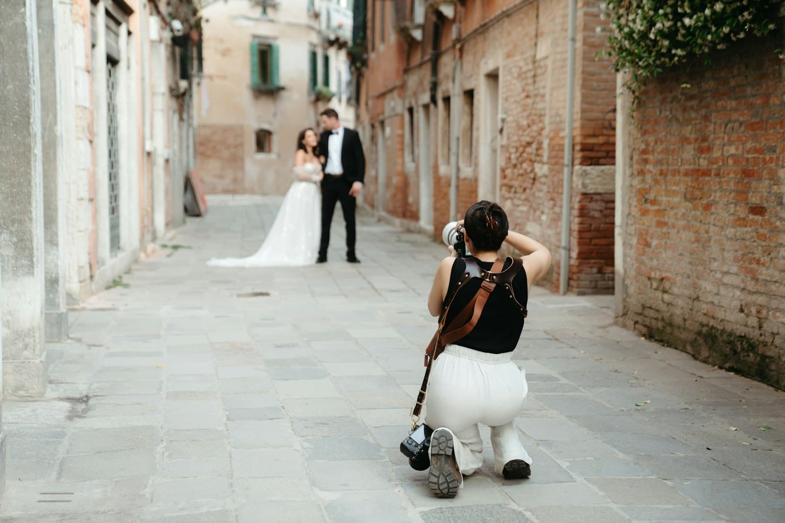 Photographer kneeling to photograph a bride and groom in a narrow street