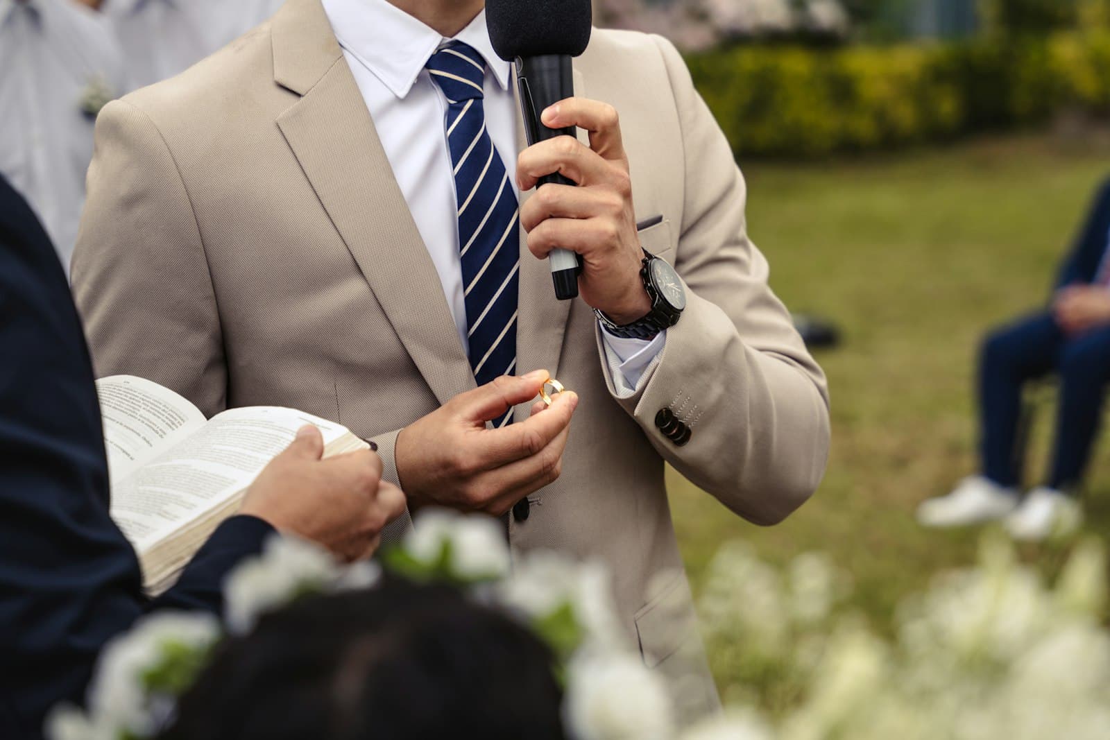 Man in a beige suit speaking into a microphone at an outdoor wedding